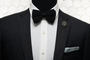 A mannequin donning a black suit jacket with Dear Martian accessories; our signature Crow Hill jet black pre-tied bow tie, Cranford rose denim pocket square, and Notorious copper beaded lapel pin.