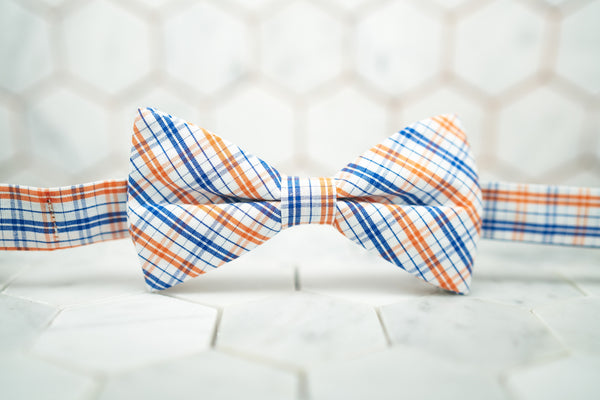 An image of the orange madras patterned bow tie sitting against a hexagon tiled background.