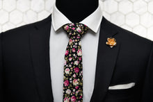 The black floral tie is paired with a rose gold rose lapel pin and a white pocket square. Displayed on a suited mannequin.