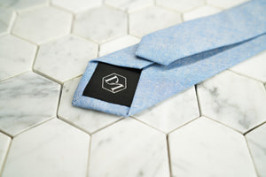 A detailed picture of the back of Dear Martian's aqua blue chambray necktie. The tipping of the tie contains the hexagonal DM logo.