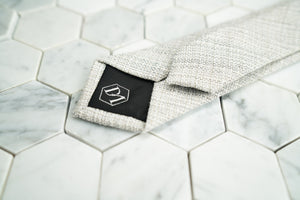 The DM hexagonal logo is shown stitched on the back of the creme men's linen skinny tie by Dear Martian.