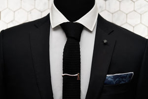 The Dear Martian, jet black tie is displayed on a mannequin, which features men's accessories such as the blue rose denim pocket square, silver axe tie clip, and skull lapel pin.