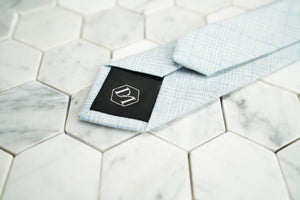 An image of the back of Dear Martian's light blue plaid skinny tie, which features the exclusive hexagon DM logo.