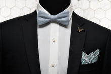A dapper mannequin dressed in a black suit jacket with Dear Martian accessories, which include; the sky blue plaid bow tie, gold stag lapel pin, and the Whitman pocket square.