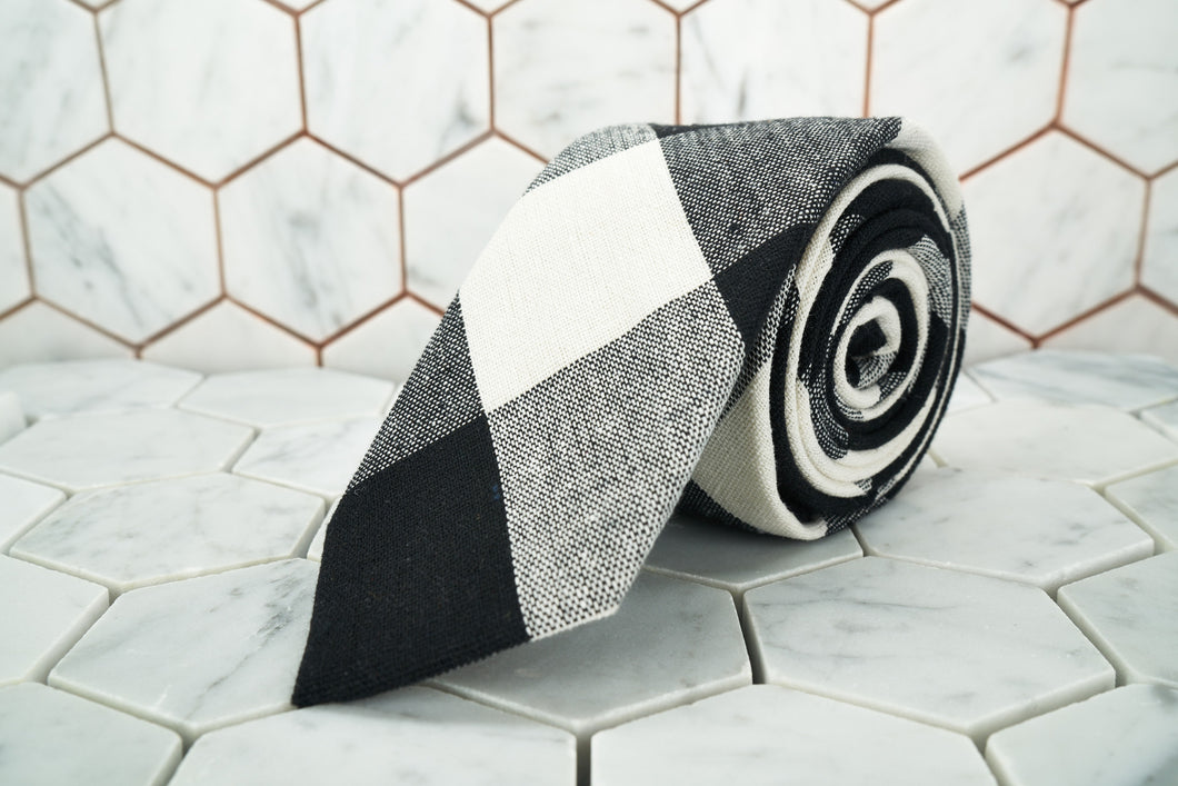 The Bobby Fischer monochrome argyle linen necktie from Dear Martian, is rolled and sitting on a hexagonal background.