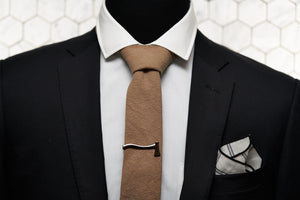 The Dear Martian brown linen tie is paired with a silver ax tie clip and Lexington white pocket square; which are featured on a mannequin wearing a black men's blazer.