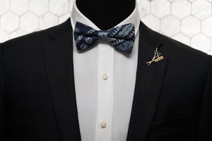An image of a mannequin in a black suit dressed with a denim blue celtic patterned bow tie, which is paired with the Fleet St. gold lapel pin by Dear Martian, Brooklyn.