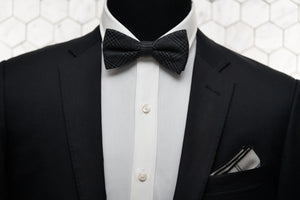 An image of a mannequin dressed in a Parisian inspired look with a charcoal grey bow tie and white argyle linen pocket square.