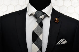 A black and white checkered tie is displayed on a mannequin. The mannequin is also wearing a black suit, Dear Martian's beaded copper lapel pin, and a black and white striped pocket square.