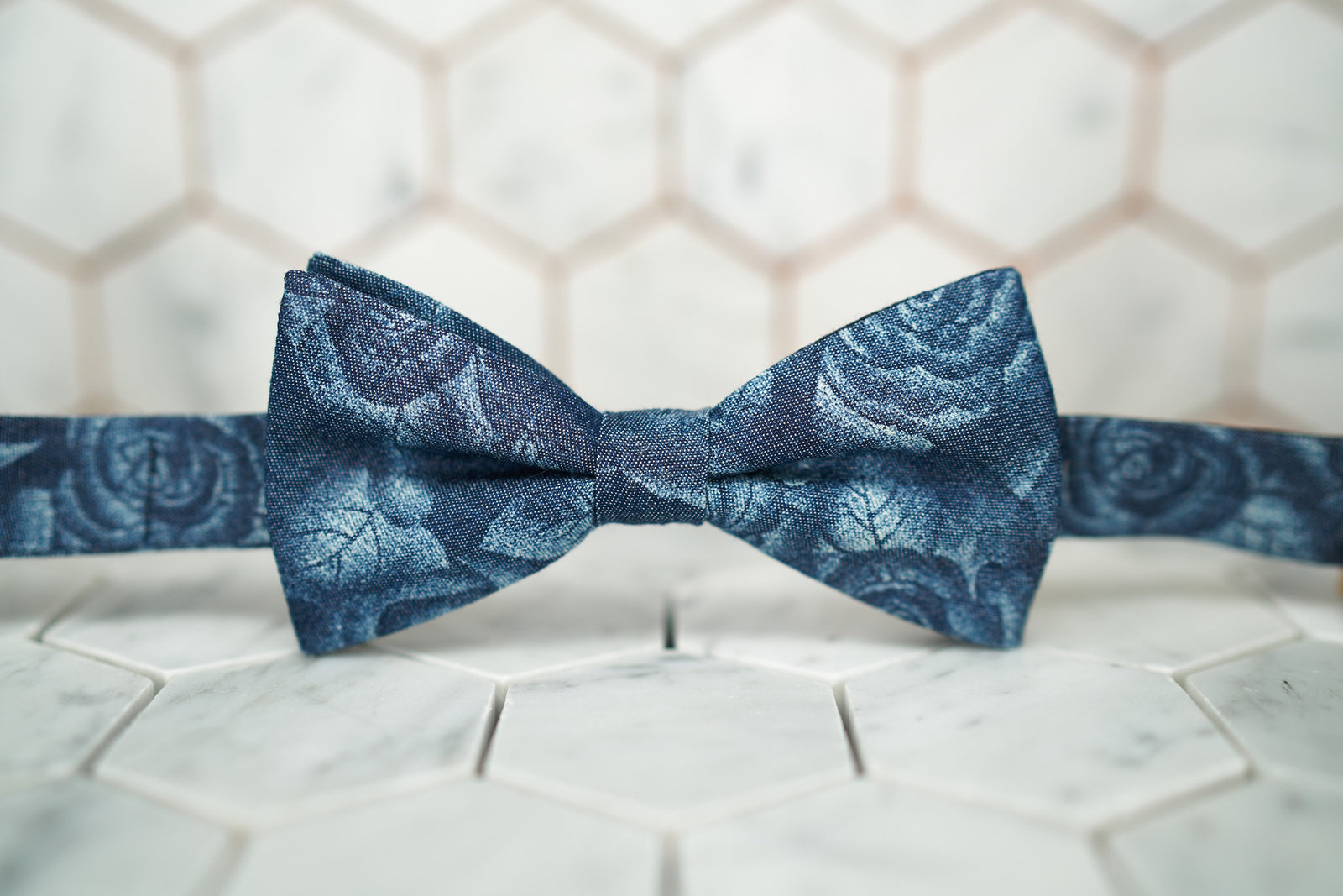 A front view of the Cranford rose denim bow tie by Dear Martian; the bow tie has light blue roses laid across its canvas.