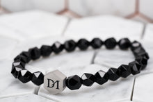 A top view image of the onyx stone chakra bead bracelet by Dear Martian Brooklyn; placed against a white tile background.
