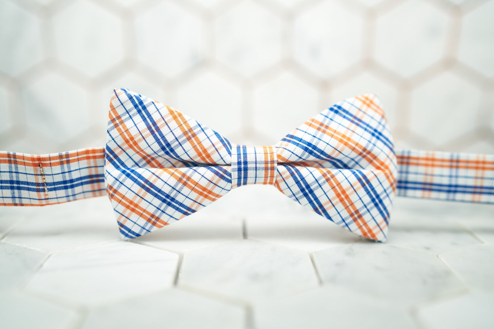 An image of the orange madras patterned bow tie sitting against a hexagon tiled background.