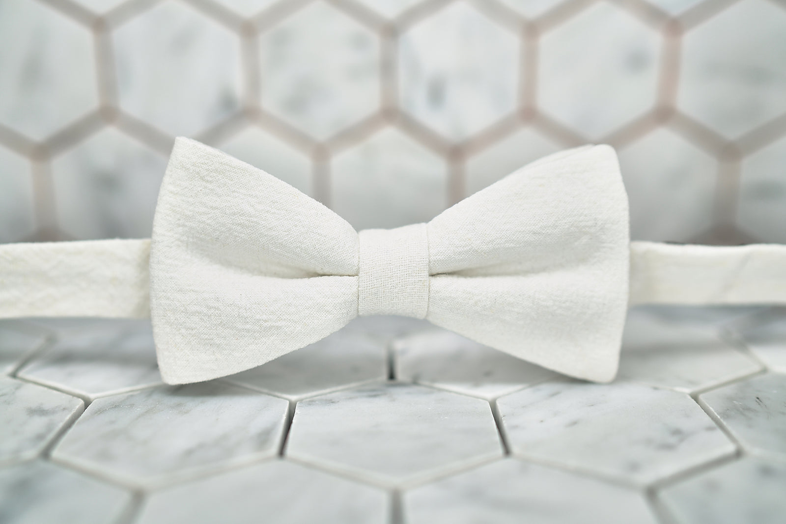 A front view of the DM Al Pacino white linen bow tie against a hexagon background.