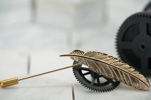 An image of a vintage gold feather lapel pin handmade by Dear Martian, Brooklyn; the suit pin sits against vintage black cogs.
