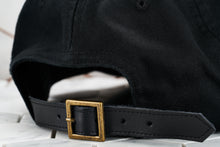 An up close image of the pointed leather adjustable strap back for the Dear Martian black hat, which features a vintage brass belt buckle.