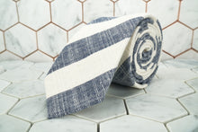 The Dear Martian grey and white striped bookie tie is rolled up  against a hexagon tiled background.