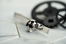 An image of Dear Martian's silver plated men's tie bar that features a skull with enamel eyes. The tie bar is facing to the left with black spray painted vintage cogs. 