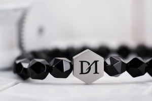 A detailed image of the steel DM logo bead strung with energy onyx stone beads to form a beautiful accessory bracelet.
