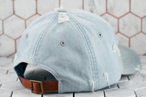 The back view of the 6 panel ripped denim blue baseball cap by Dear Martian, which shows the light brown leather adjustable strap.
