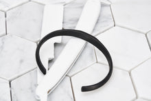A top view product image of Dear Martian's pvd matte black cuff bracelet sitting against a white razor blade.