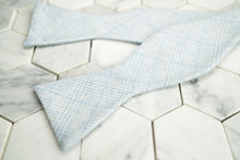 An image of Dear Martian's Tiffany blue glen plaid bow tie untied, lying against a hex tiled background.