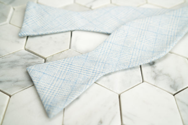 An image of Dear Martian's Tiffany blue glen plaid bow tie untied, lying against a hex tiled background.