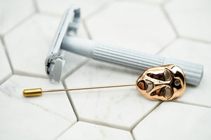 An image of the tragedy gold costume mask boutonniere laying against a vintage white spray painted razor.