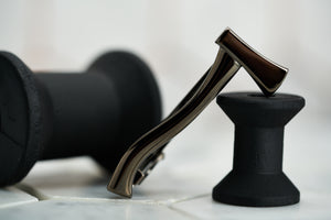 An image of the Dear Martian gunmetal axe tie bar tie clip; laying on a black spray painted spool.