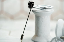 A front image of the Dear Martian gunmetal skull lapel pin lying against a wooden spool.