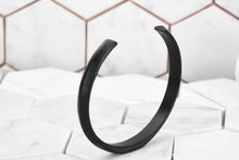 An image of the Duality matte black cuff bracelet for men facing up with a white hexagon background.
