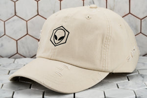 The front view of the ripped up stone khaki martian cap, which features a black embroidered hexagon encompassing an alien.