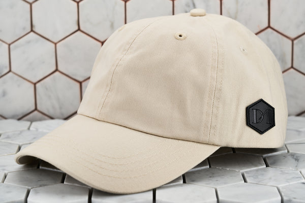A front image of the stone khaki cotton twill hat by Dear Martian Brooklyn, which portrays the hexagonal leather DM patch logo.