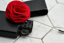 A side image of the salsa red floral lapel pin laying across a black vintage zippo lighter.