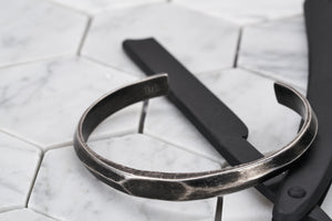 A product image of the Duality antique steel bangle bracelet sitting on top of a matte black painted straight edge razor. 