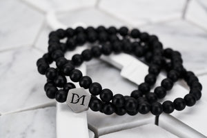 An image of the the white howlite wrap stone bracelet on top of a white spray painted straight edge razor. The beads are matte black with a steel hexagon logo bead.