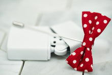 An image of a red polka dotted bow tie lapel pin; sitting on top of a vintage white lighter.