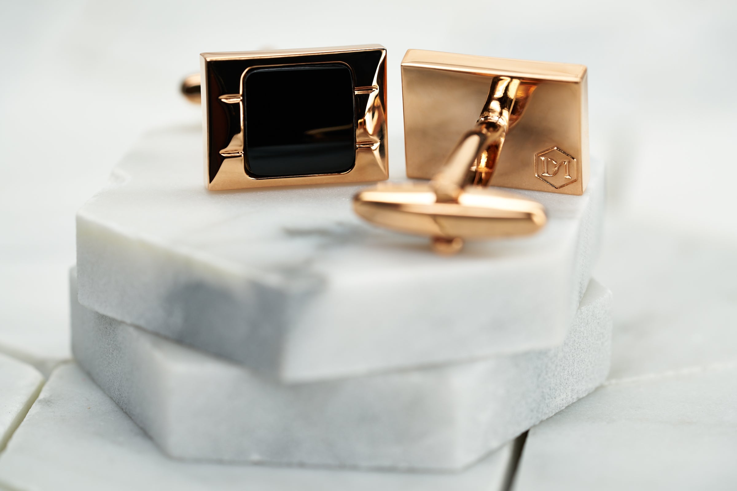 A product image featuring a pair of rose gold cufflinks by Dear Martian. The image depicts the front side, which has a solid black enameled center and the back of the cufflink, which shows the DM hexagon logo.
