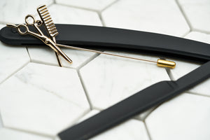 A product image of the gold lapel pin named Fleet Street by Dear Martian, Brooklyn. This stylish barber lapel pin is plated with gold and lying against a straight razor.
