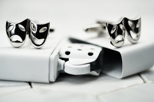 A pair of silver plated costume masquerade mask cufflinks made by Dear Martian sitting on top of a vintage spray painted zippo lighter.