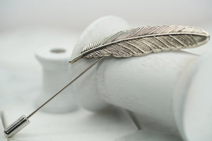 An image of the Dear Martian, Veder; vintage steel feather lapel pin laying against a wooden spool.
