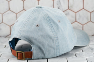 The back view of the Dear Martian solid denim blue dad hat , which shows of the brass buckle adjustable strap closure.