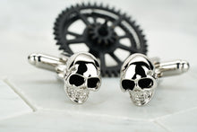 A pair of steel skull cufflinks with enamel eyes made by Dear Martian, Brooklyn. These cufflinks sit against a white hexagonal background.