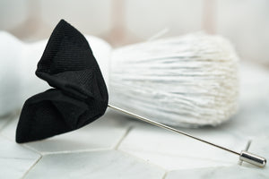 An image of a black butterfly boutonniere pin against a vintage white beard brush by Dear Martian.
