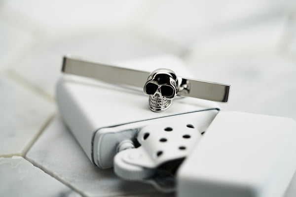 An image of a stainless steel men's skull tie clip handmade from Dear Martian. The tie bar is sitting a top a white spray painted vintage zippo lighter.
