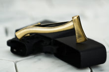 A product image of the antique gold kloven axe tie bar by Dear Martian, Brooklyn; which lays upon a black zippo lighter.