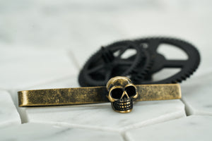 An photo of the vintage brass skull tie bar from Dear Martian, which lays against a white hexagonal background.