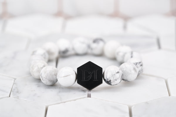 A front view image of the Dear Martian white howlite stone beaded bracelet with a black hexagon logo bead. The beaded bracelet is sitting on a white background.