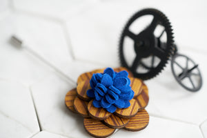 An image of a floral wooden lapel pin with a felt wool blue center by Dear Martian, Brooklyn.