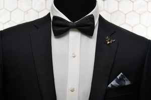An image of a mannequin dressed dapper in our Strauss Raw bow tie paired with; a gold stag lapel pin, and camo blue denim pocket square.