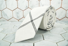 The Ghost White argyle linen necktie made by Dear Martian is rolled up  and lying on a hexagon tiled background.
